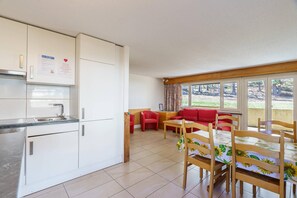 A compact kitchen with white cabinets and a dining area with a red sofa and wooden chairs. - Comfortable 2 Bedroom Apartment with Mountain Views Haus Alfa (Saas Fee)