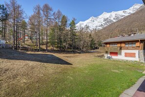A chalet with a wooden balcony, a grassy yard, and a mountain backdrop. - Cozy 2-Bedroom Apartment with Mountain Views at Haus Alfa (Saas Fee)