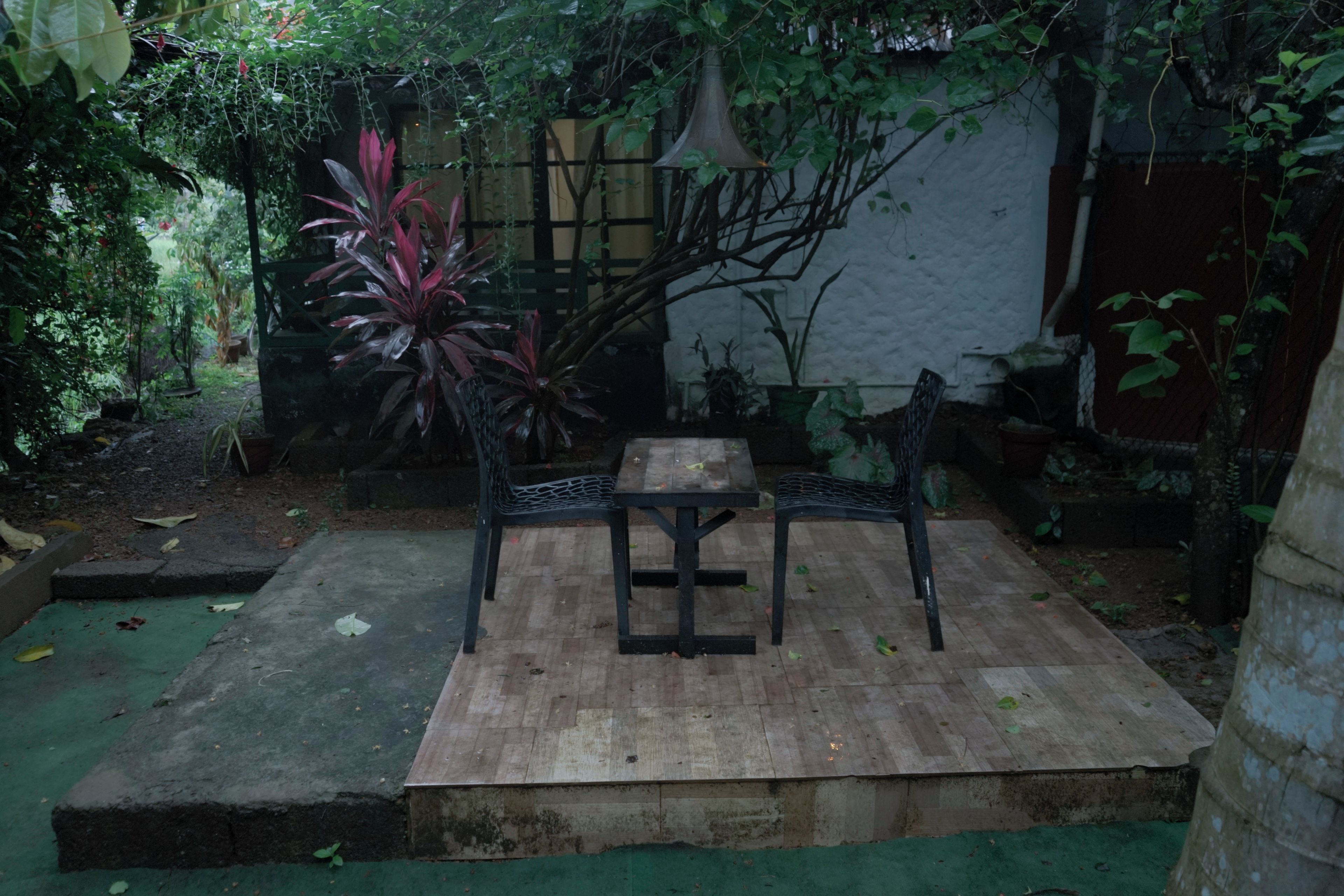 Een buitenzitplaats met een tafel en stoelen, omgeven door planten en een houten terras.