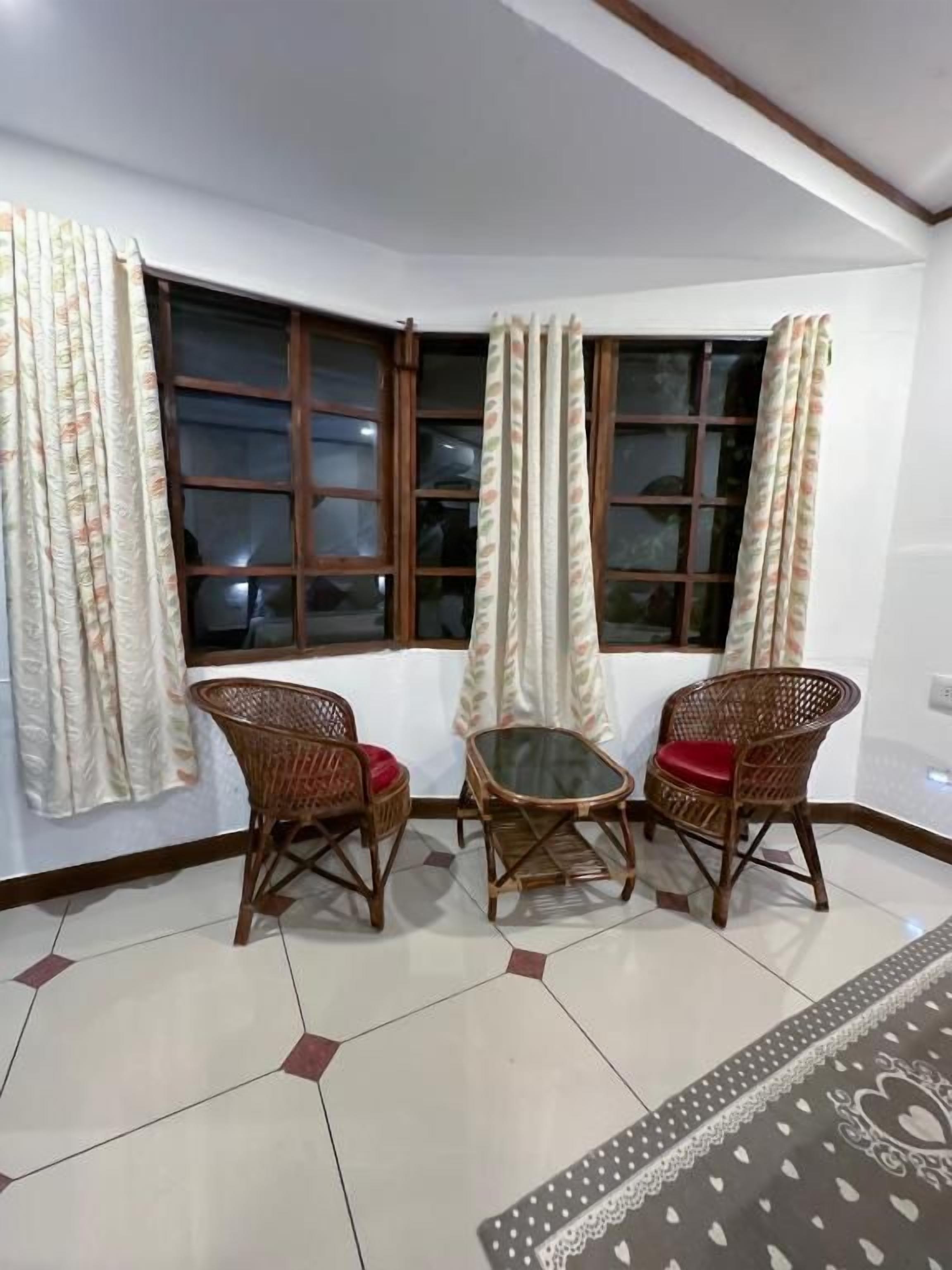 Una habitación en esquina con ventanal saliente, dos sillones de mimbre, una mesita y una alfombra estampada.