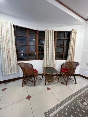 A corner room with a bay window, two wicker chairs, a small table, and a patterned rug. - Riverdale Homestay Kumarakom by LexStays (Arpookara)