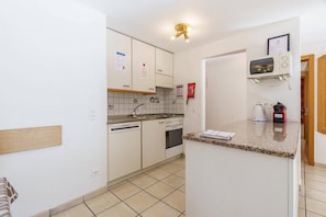 Una cocina compacta con armarios blancos, horno integrado y una pequeña encimera.