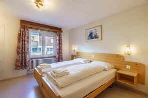 Une chambre d’hôtel avec un lit double, une tête de lit en bois, une table de chevet, une lampe fixée au mur et une fenêtre avec des rideaux.
