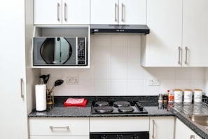 Cozinha moderna com armários brancos, bancada preta, micro-ondas embutido, fogão e coifa.
