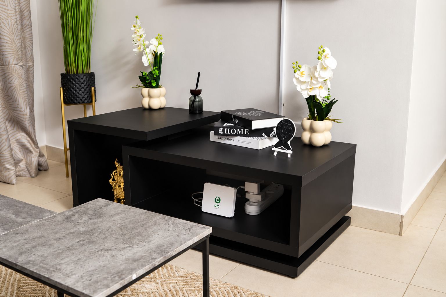 A modern living room with a black entertainment unit, a small table, and decorative plants.
