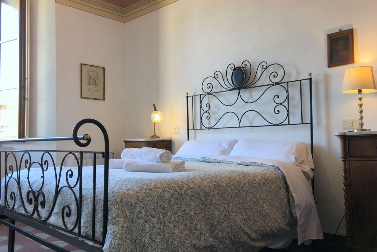 Ein ordentlich bezogenes Bett mit einem Metall-Kopfteil, einer Nachttischlampe und einem gerahmten Bild an der Wand.