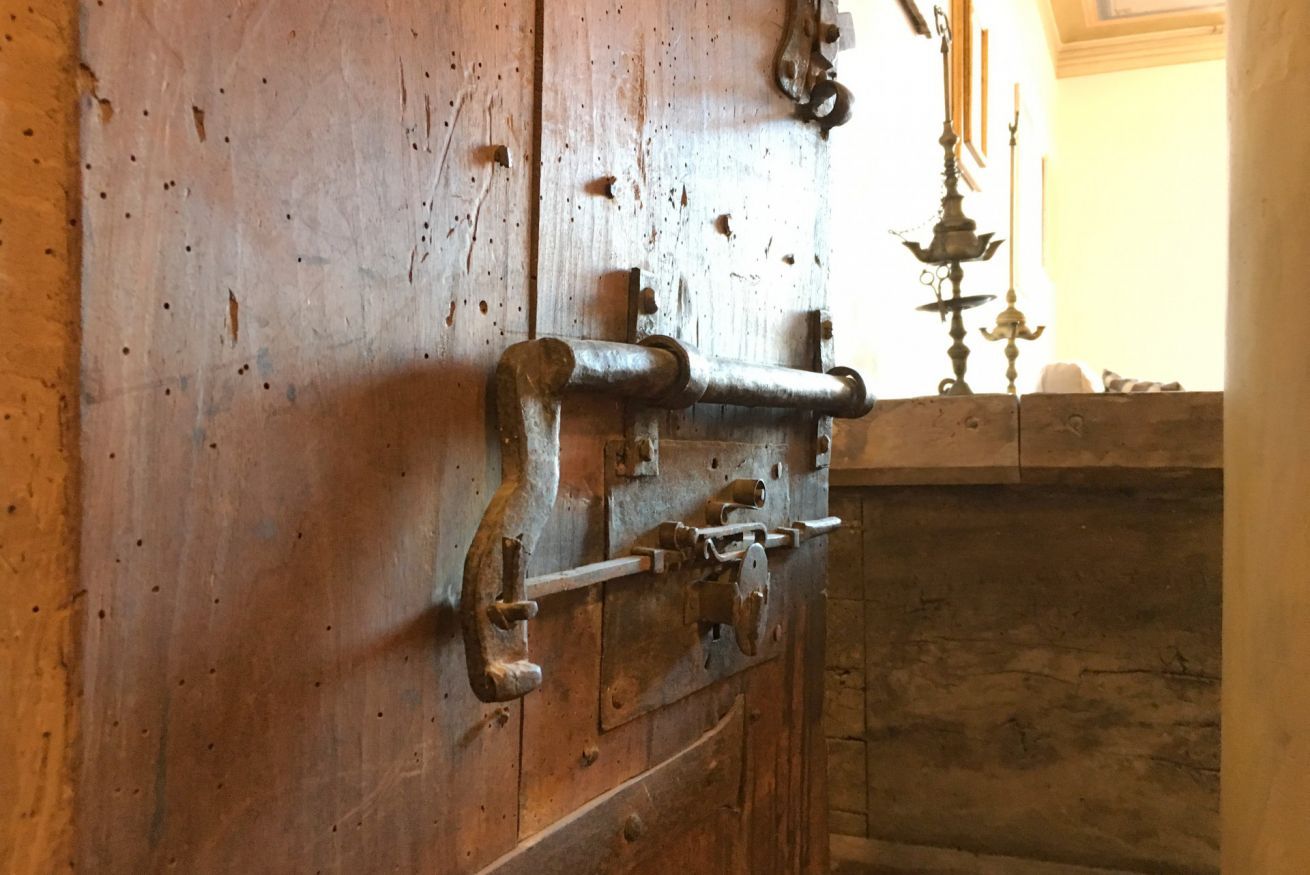 Una porta in legno rustica con un chiavistello in metallo e un elemento decorativo in metallo sulla parete.