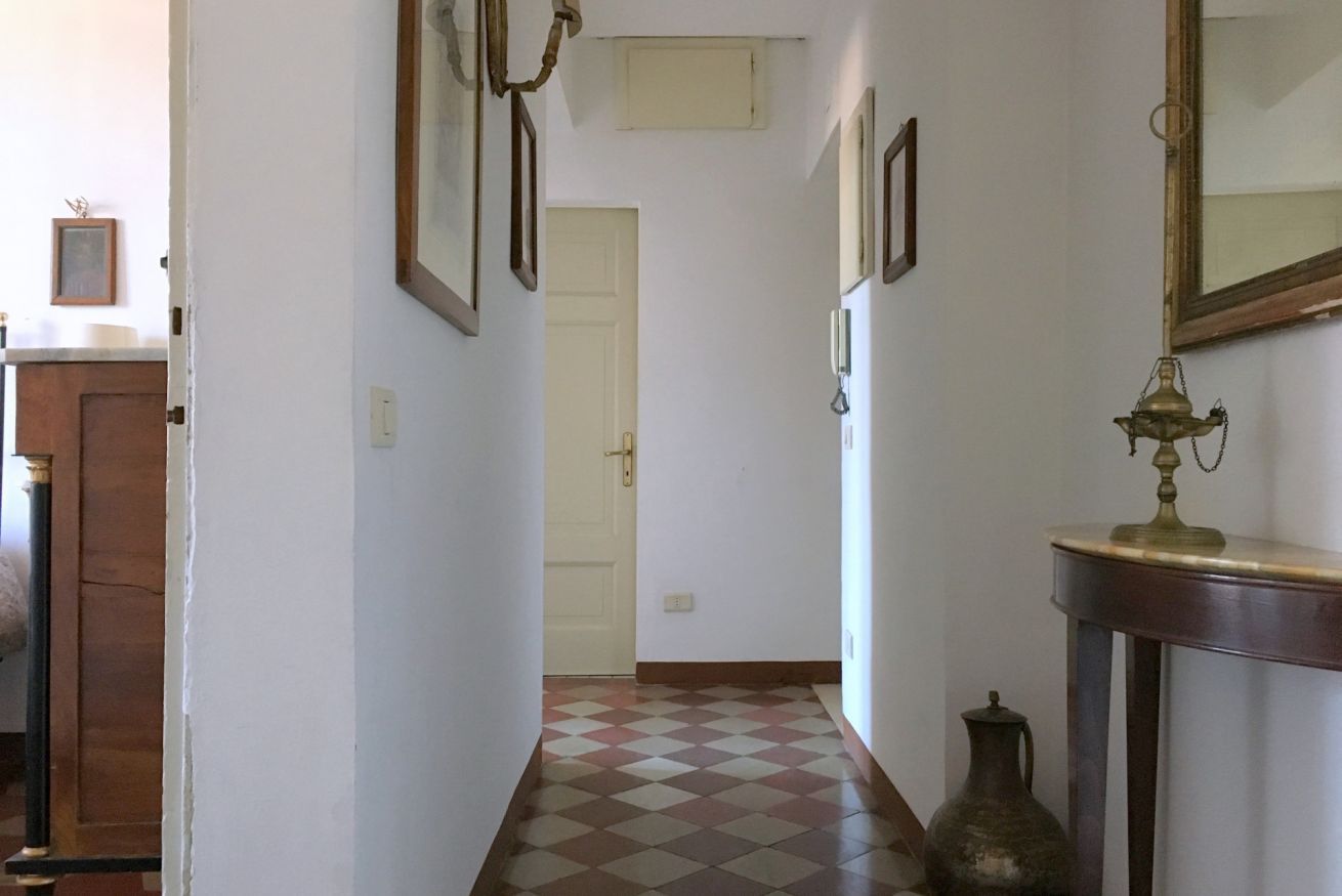 Un corridoio con pavimento a scacchi, una porta in fondo e uno specchio a parete.