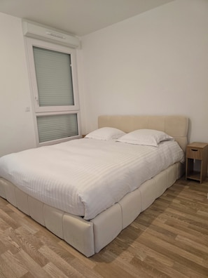 Ein Schlafzimmer mit einem Bett, einem Nachttisch, einem Fenster mit Jalousien und Holzboden.