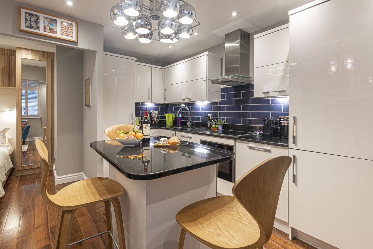 A modern kitchen with white cabinets, a black countertop, and two wooden bar stools.