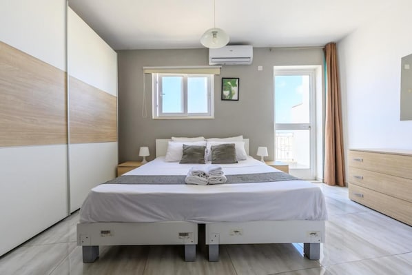 Une chambre à coucher moderne, équipée d’un lit, de tables de chevet, d’une fenêtre, d’un climatiseur et offrant une vue sur l’extérieur.