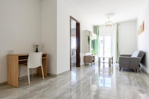 Un salon moderne avec un bureau en bois, une chaise blanche, un canapé gris et une petite table.