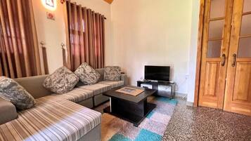 A living room with a sofa, a coffee table, a television, and a wooden door.