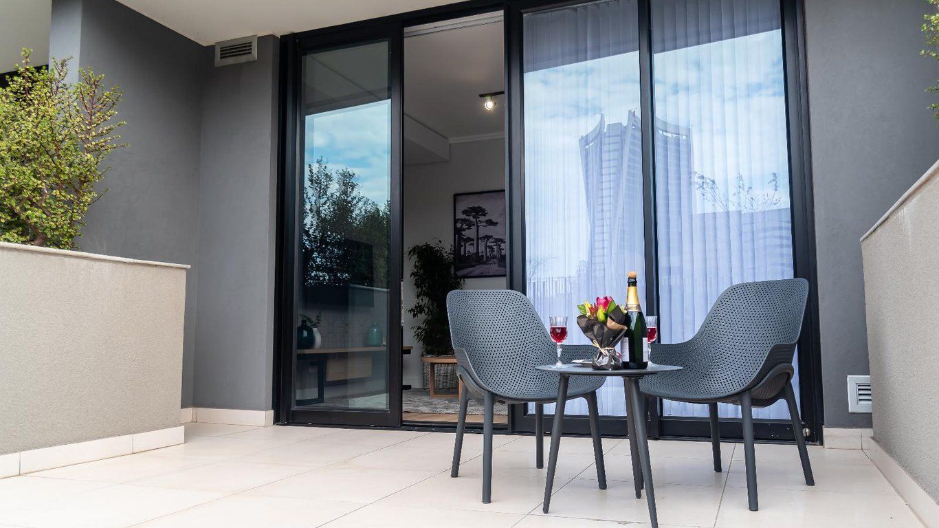A balcony with two chairs and a table, a bottle of champagne, and a vase with flowers.