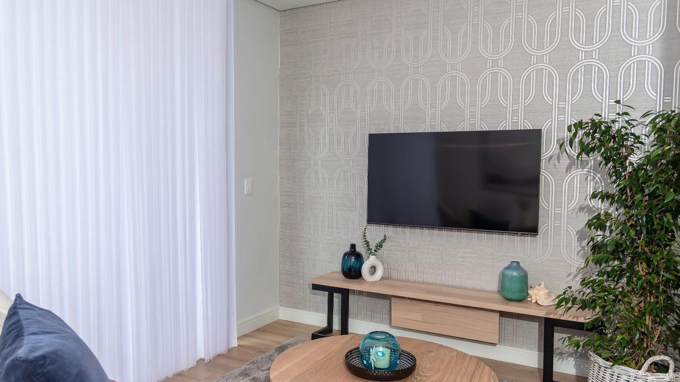 Un salon moderne avec un téléviseur à écran plat fixé à un mur texturé, une table basse en bois agrémentée d’objets décoratifs et une plante en pot.