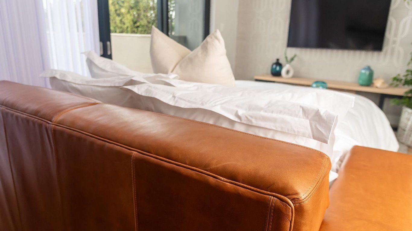 Een bed met witte lakens, een bruin lederen hoofdbord en een nachtkastje met een blauwe vaas.