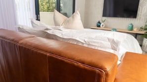 Ein Bett mit weißer Bettwäsche, einem braunen Leder-Kopfstück und einem Nachttisch mit einer blauen Vase.