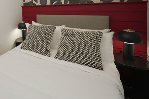 Een bed met gestreepte kussens, een rode hoofdbord en twee bedlampen.