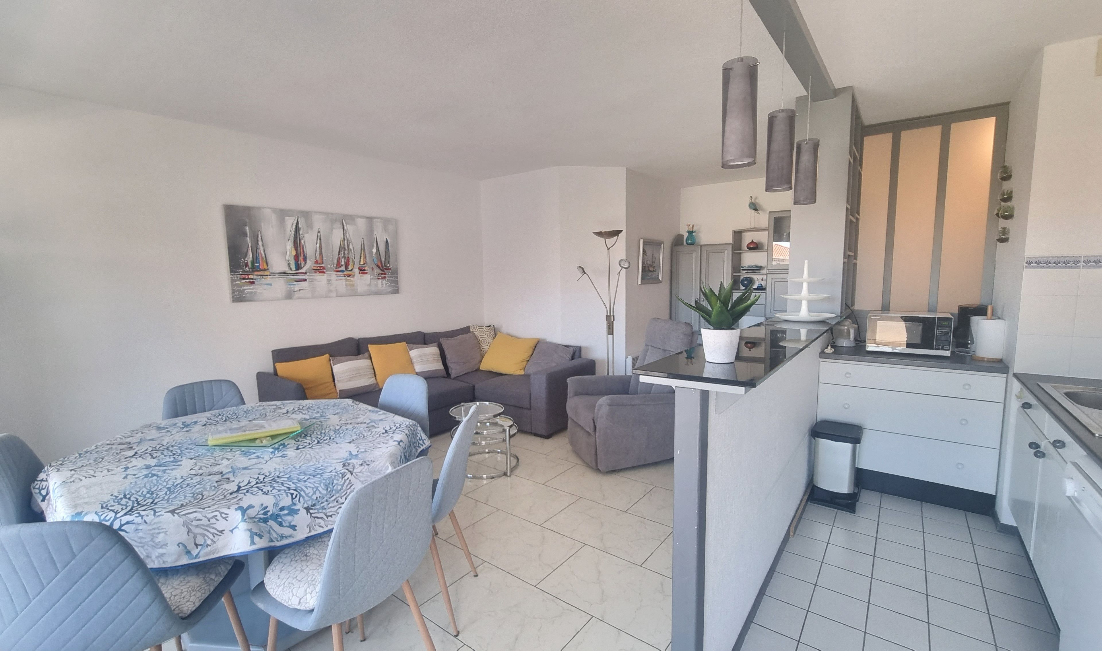 A compact living space with a dining area, a sofa set, a kitchen with modern appliances, and a decorative painting on the wall.