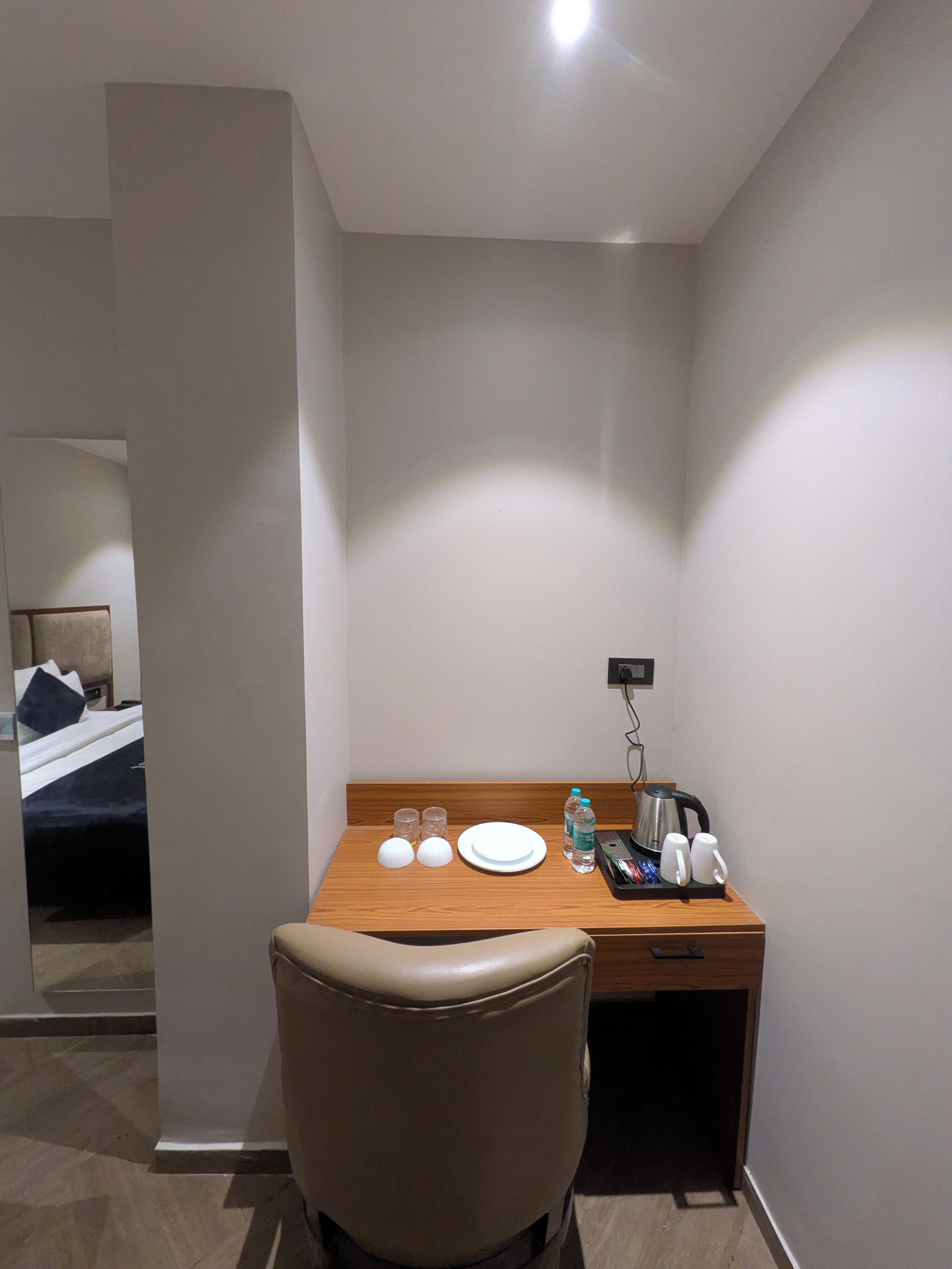 Una habitación de hotel con un escritorio de madera, una silla, una cama y una mesita de noche con una lámpara.