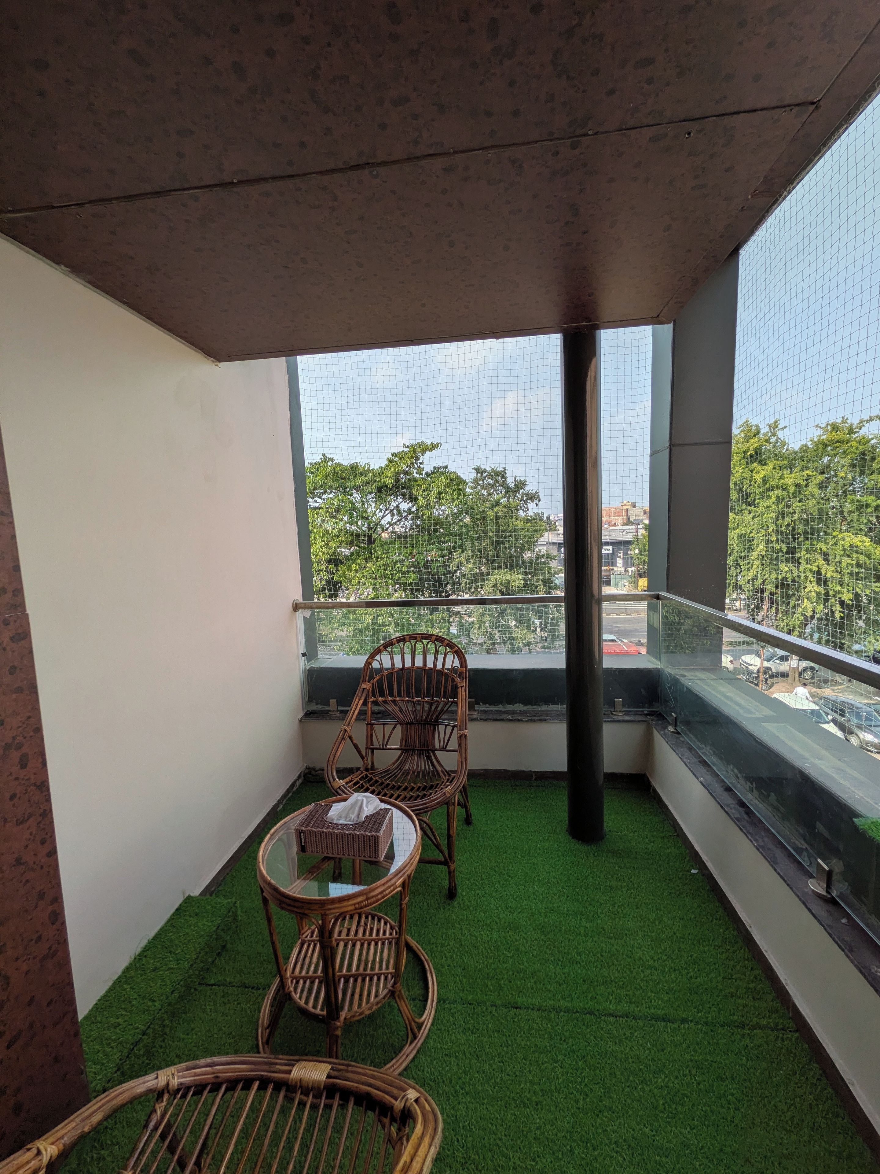 Un balcón con césped artificial verde, mobiliario de mimbre y vistas a un paisaje urbano.