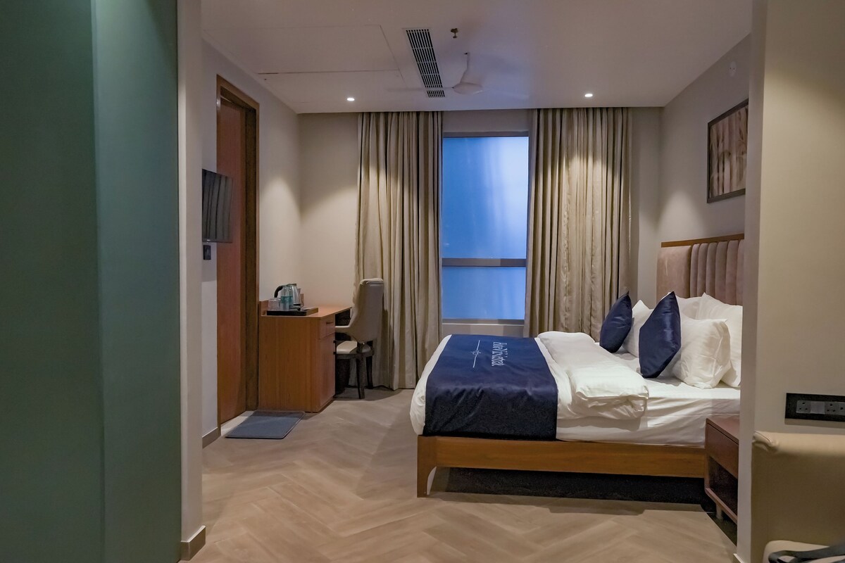 A hotel room with a bed, a desk, a chair, and a window with curtains.