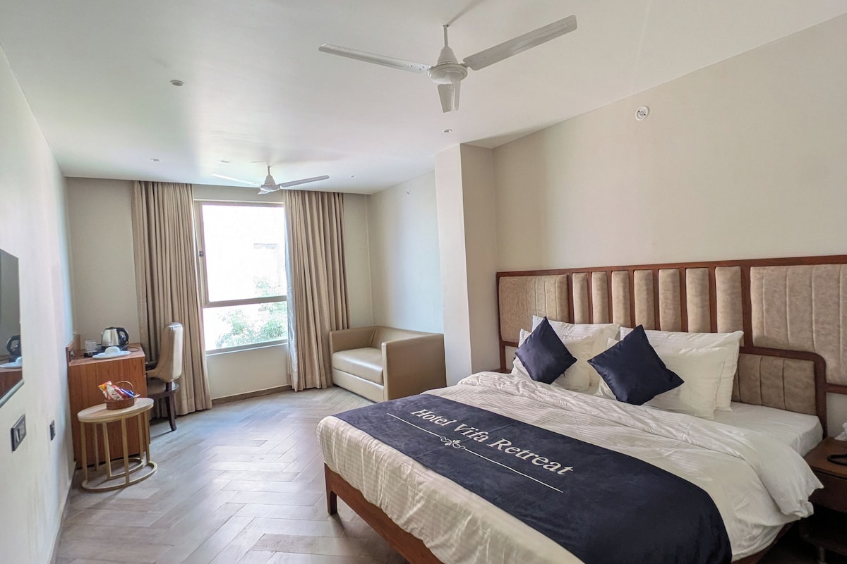 A hotel room with a bed, a desk, a chair, a ceiling fan, and a window with curtains.