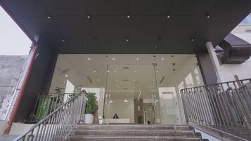 Una escalera conduce a un área de recepción con puertas de vidrio, barandilla metálica e iluminación empotrada en el techo.
