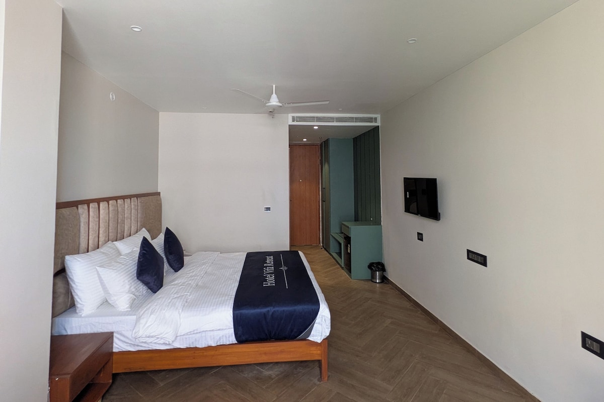 A hotel room with a bed, a ceiling fan, a television, and a wooden floor.