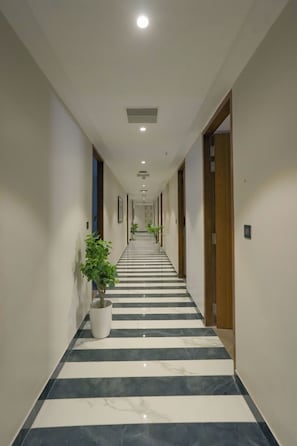 A hotel corridor with a striped floor, doors on both sides, and potted plants. - Hotel Vifa Retreat (Lucknow)
