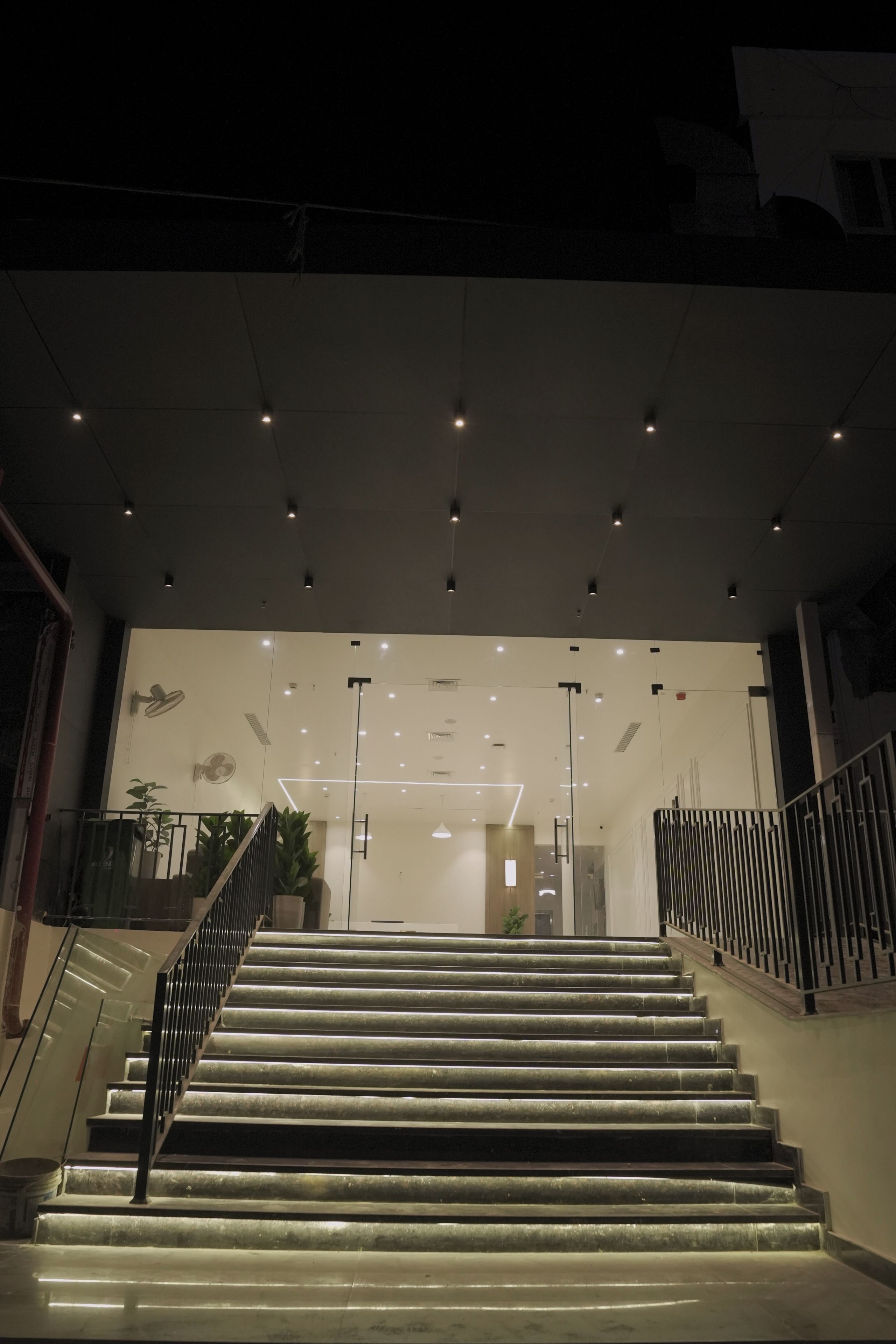 Una escalera conduce a la entrada de un edificio de diseño moderno, con un puerta de cristal y una barandilla metálica.