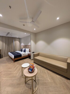A hotel room with a bed, a sofa, a small round table with snacks, and a ceiling fan. - Hotel Vifa Retreat (Lucknow)
