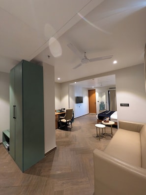 A hotel room with a large wardrobe, a sofa, a desk with a chair, and a television. - Hotel Vifa Retreat (Lucknow)