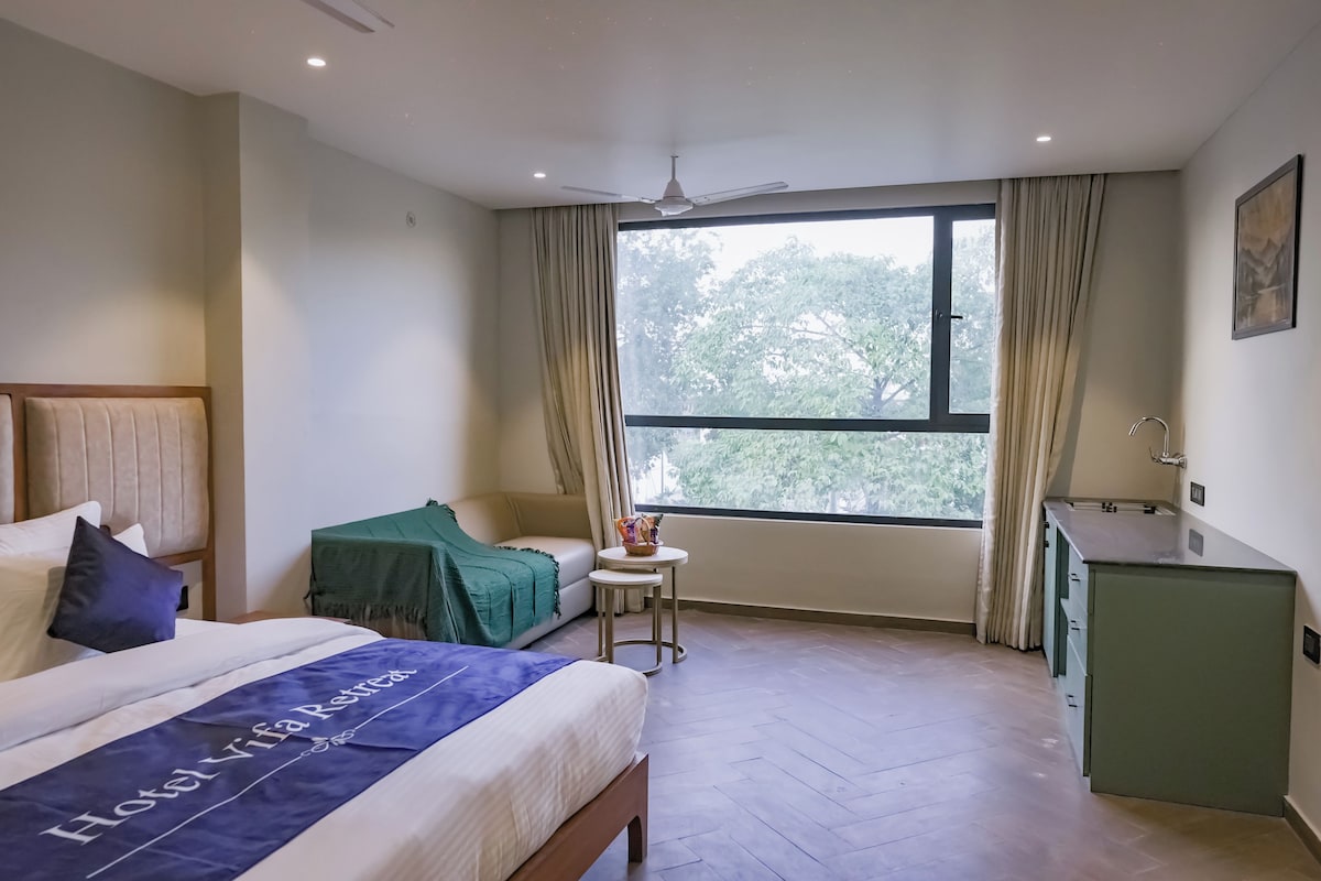 A hotel room with a bed, a small table, a desk, a window with curtains, and a ceiling fan.