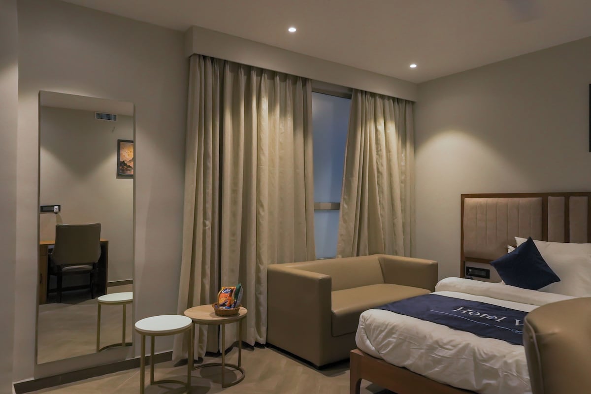 A hotel room with a bed, a chair, a small table, and a mirror.