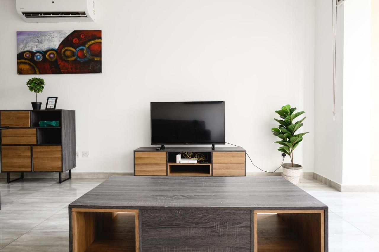 Un salon moderne avec un téléviseur à écran plat posé sur un meuble en bois, une table basse au centre et une plante en pot sur la droite.