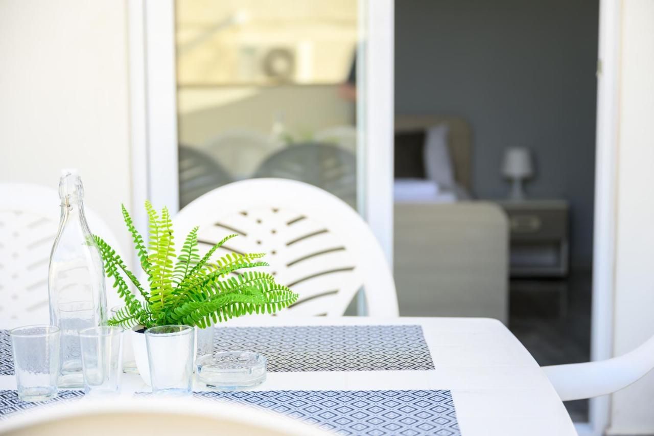 Ett bord med ett mönstrat bordsduksöverdrag, en genomskinlig glasflaska, en krukväxt av typen ormbunke och flera glas.