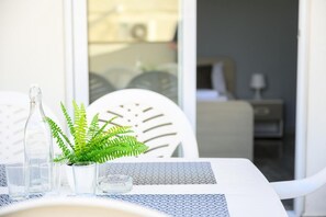 Una mesa con mantel estampado, una botella de vidrio transparente, una heleadera en maceta y varios vasos.