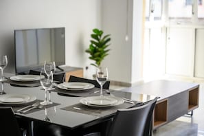 Un comedor con una mesa larga dispuesta para cuatro personas, con platos, cubiertos y copas de vino.