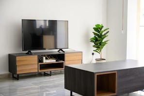 Una sala de estar moderna con un televisor de pantalla plana sobre un mueble de madera, una planta en maceta y una mesa de centro minimalista.