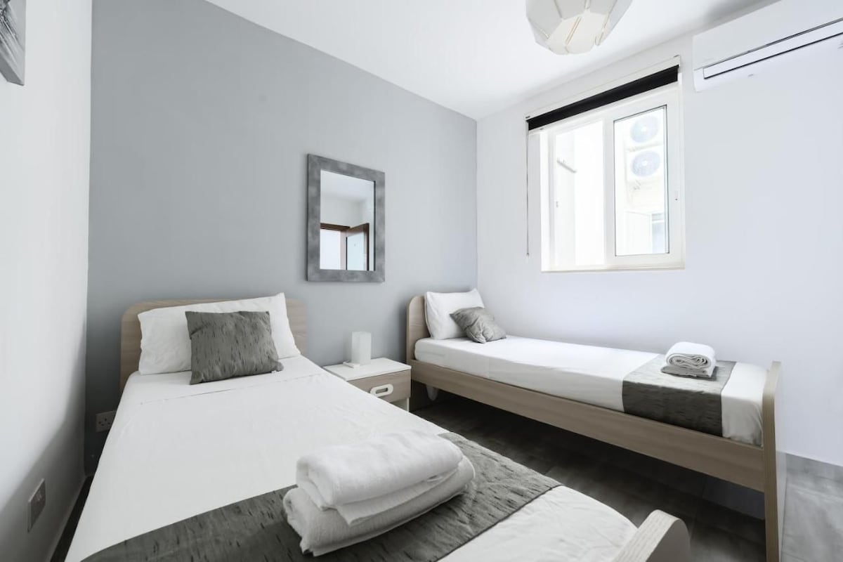 Ein modernes Schlafzimmer mit zwei Betten, einem großen Spiegel und einem Fenster mit Jalousien.