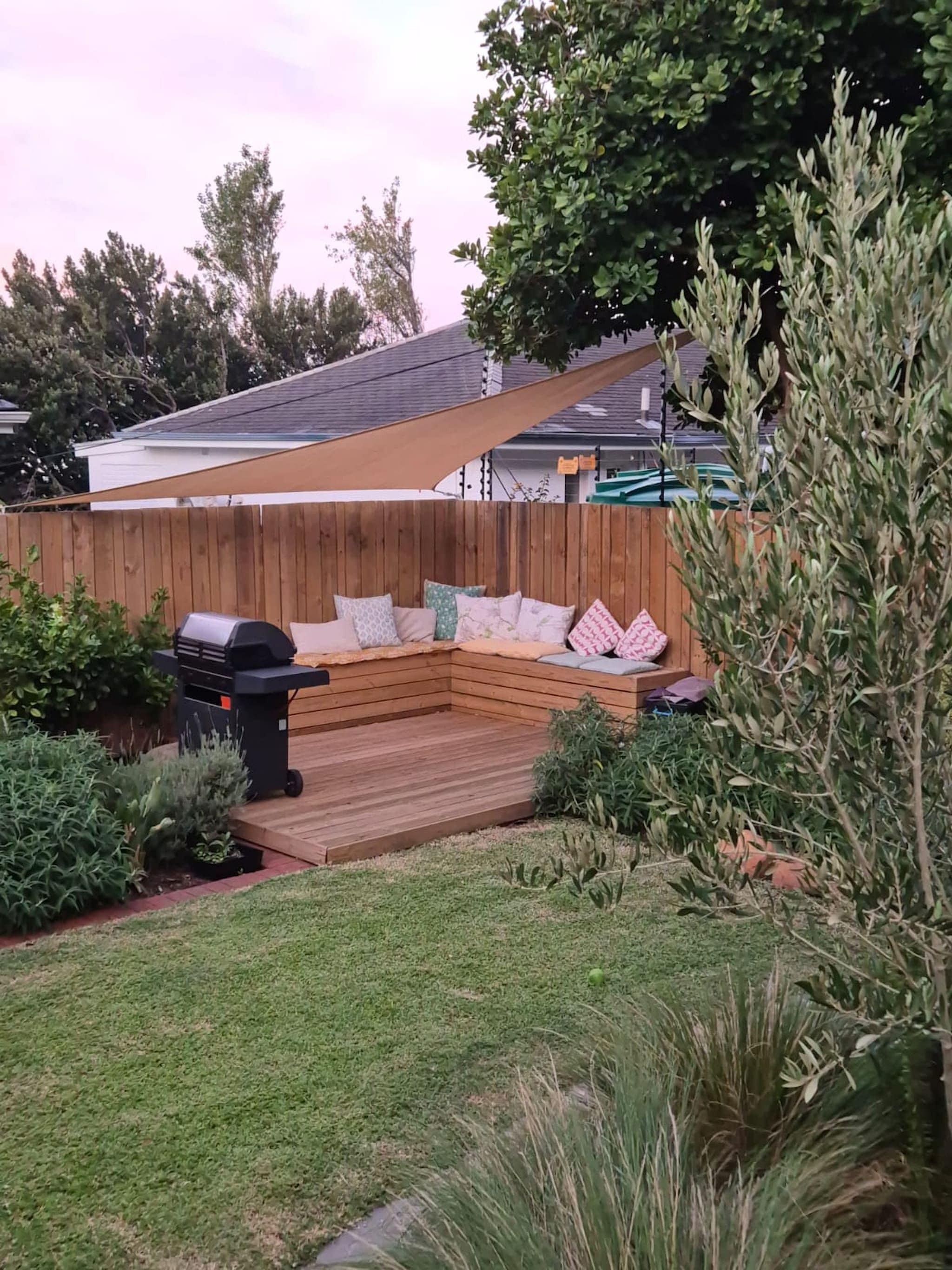 Un patio trasero con una terraza de madera, una parrilla y una zona de estar con cojines.