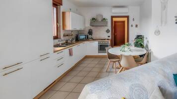 Una cucina compatta con mobili bianchi, un forno a microonde e una zona pranzo con un tavolo rotondo e sedie.
