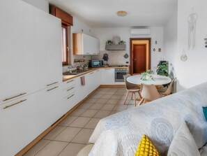 Cozinha compacta com armários brancos, micro-ondas e área de refeições com mesa e cadeiras redondas.