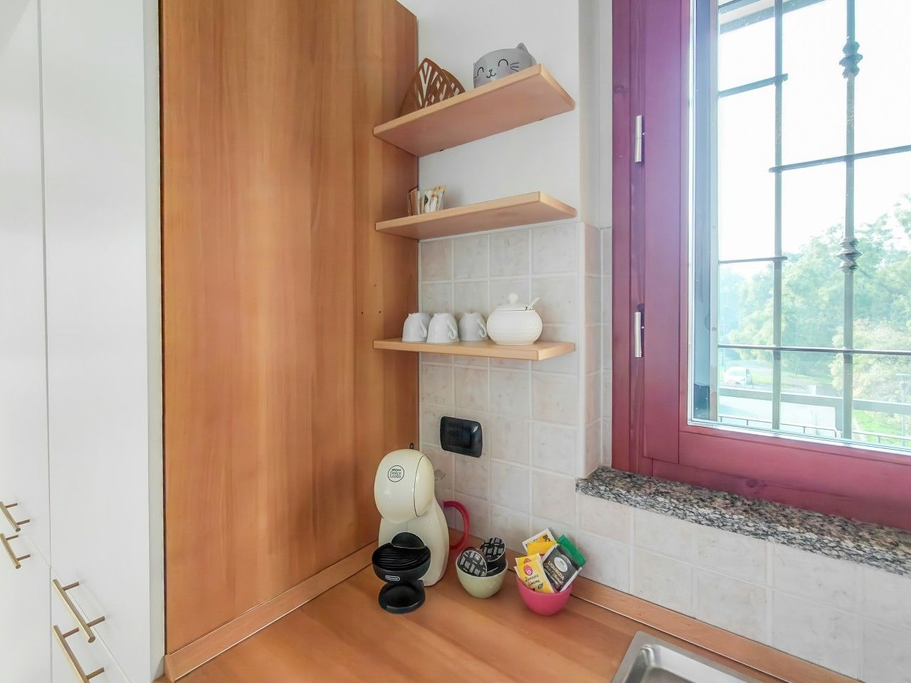 A compact kitchen with wooden cabinets, a window with a view, and a countertop with various items.