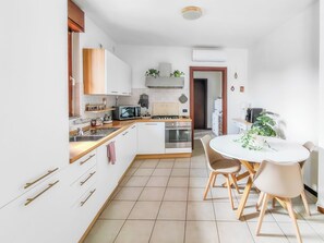 A modern kitchen with white cabinets, a microwave, stove, and a dining area with a table and chairs. - Casa Laura (Milano)
