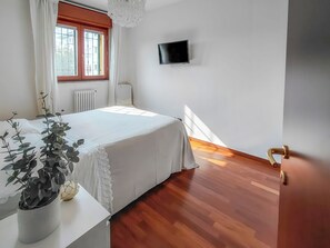 A bedroom with a bed, a television on the wall, a window with curtains, and a potted plant. - Casa Laura (Milano)