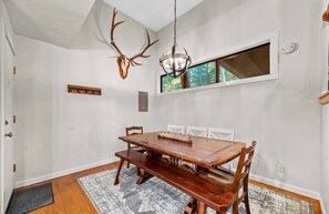 A dining area with a wooden table and chairs, a hanging light fixture, and a deer skull mounted on the wall. - Spacious Sugarbush Mtn Retreat, Fireplace, Loft & Ski Room, Sleeps up to 8 (Warren)