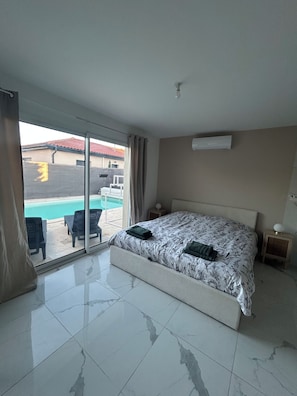 A hotel room with a bed, a sliding glass door to a pool area, a bedside table, and a nightstand.