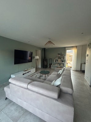 A modern living room with a large sofa, a flat-screen TV, a coffee table, and a bookshelf. - New Listing (Blyes)